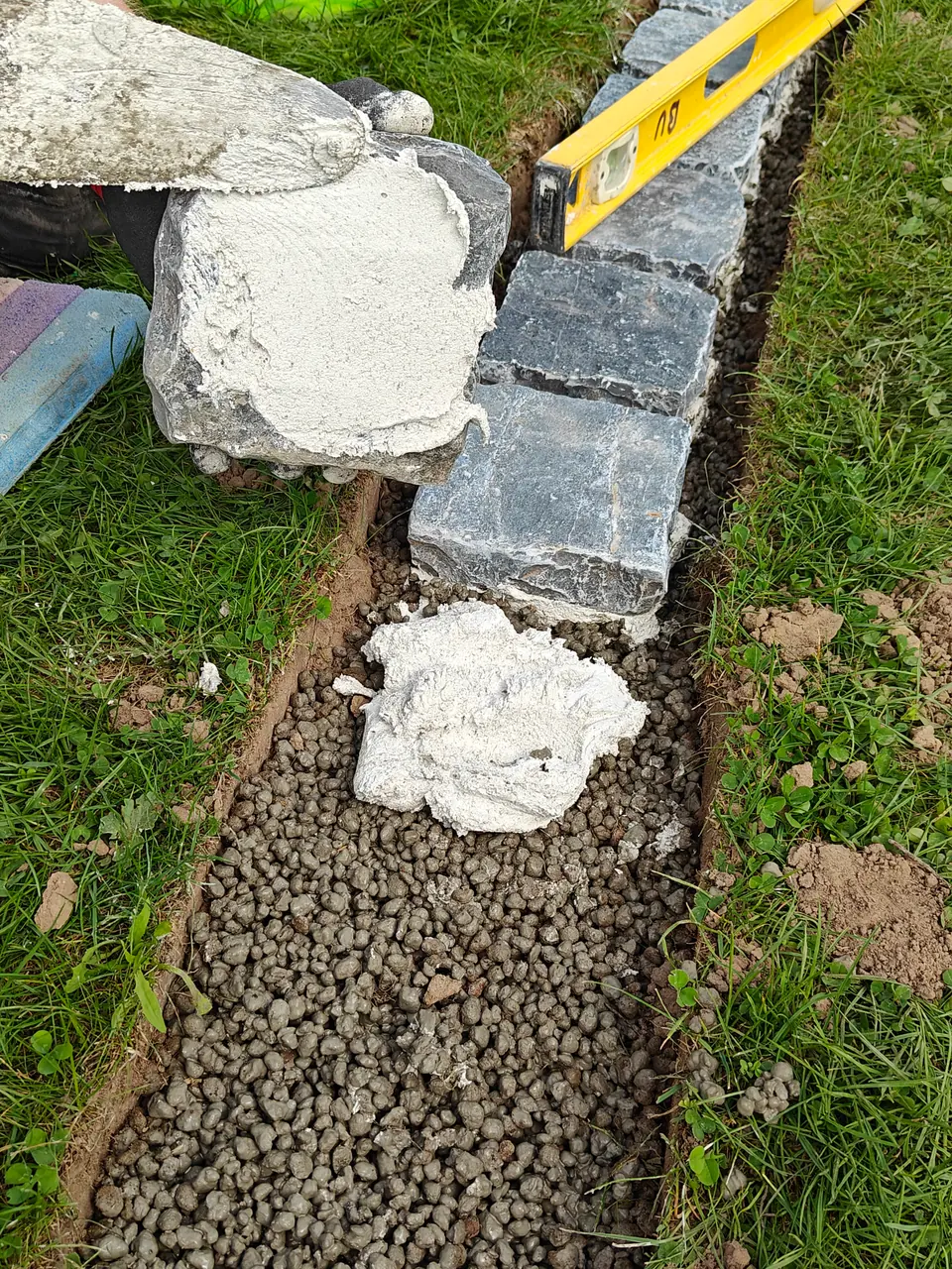 Colle à carrelage blanche sur le lit de pose et sous le pavé en pierre naturelle